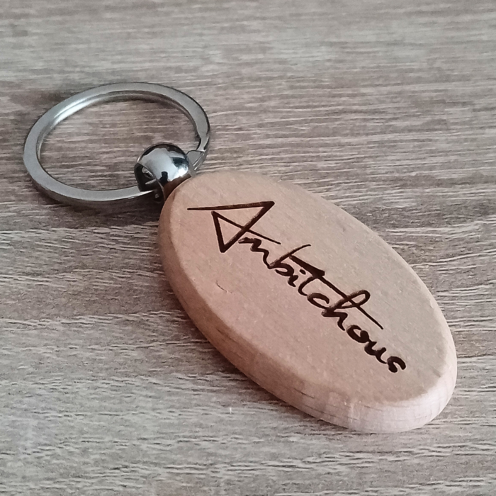 Wooden keychain with Ambitchous engraving placed on a wooden surface