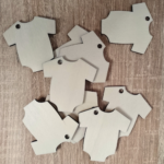 A collection of plywood baby onesie tags spread out on a wooden surface