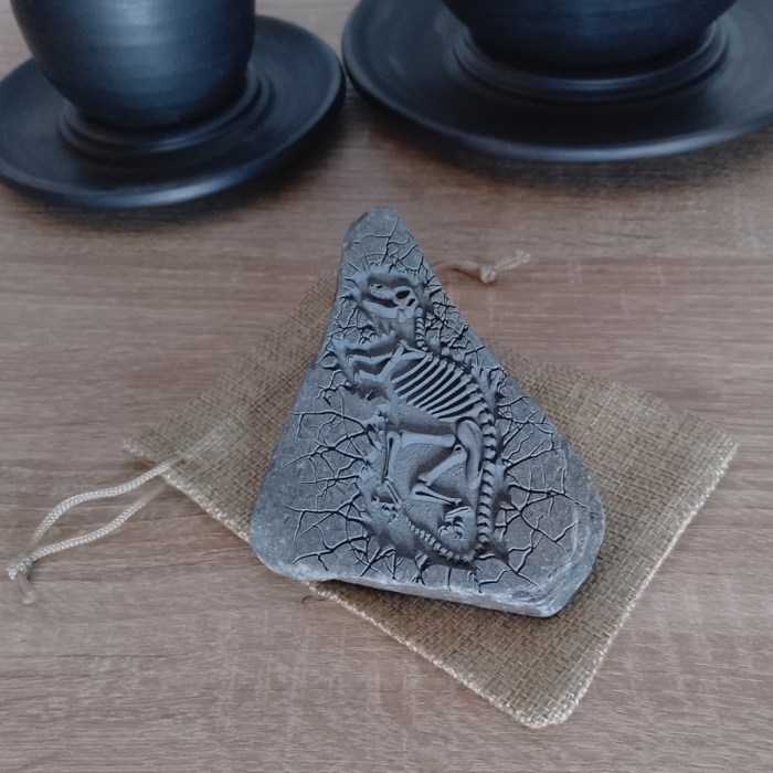 Engraved dinosaur fossil stone displayed on a rustic burlap pouch, perfect for gifting.
