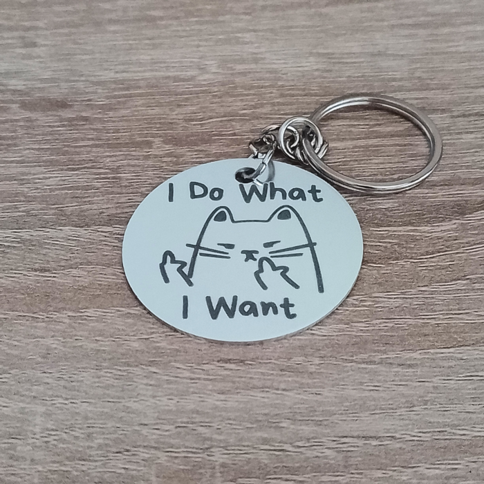 Silver aluminium keychain with I Do What I Want cat design placed on a wooden surface