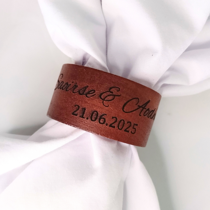 A close-up of a personalised engraved napkin ring on a white napkin, featuring names and a date.