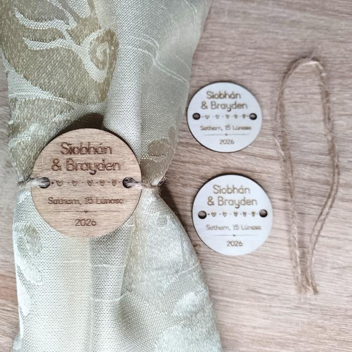 Laser-engraved wooden napkin tags tied around a napkin, with oak-stained and unfinished wood finishes.