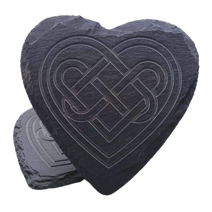 A heart-shaped engraved slate coaster with an intricate Celtic knot design, standing upright against another coaster.