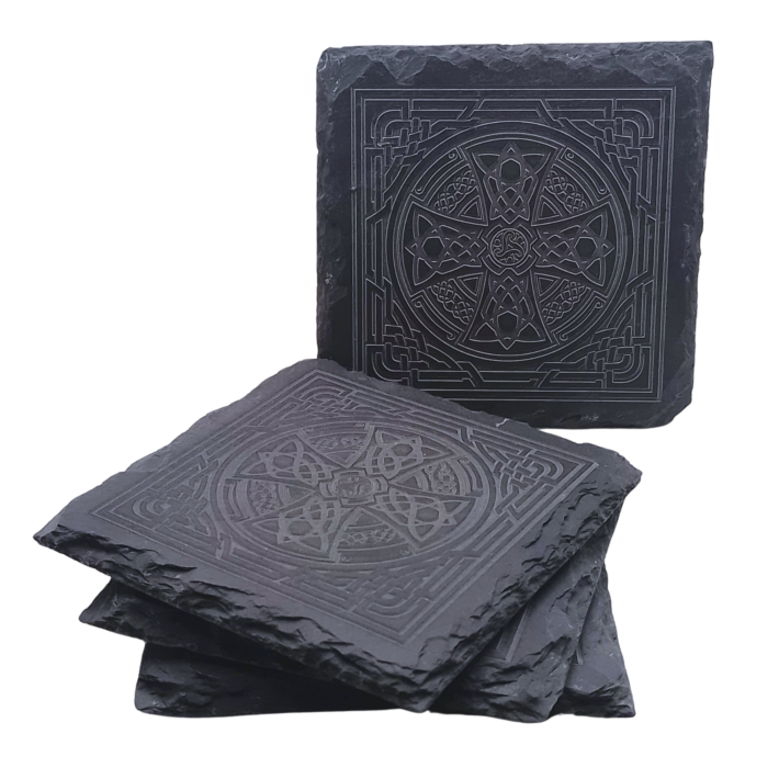 A square slate coaster engraved with a Celtic Cross design, displayed upright with other coasters stacked beneath.