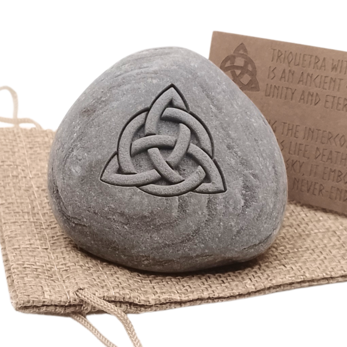 Engraved Triquetra stone placed on a natural burlap gift pouch, with an explanation card detailing the meaning of the Triquetra symbol.
