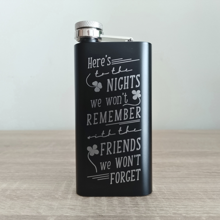 Black coated stainless steel custom flask with engraved funny Irish toast, front-facing on table.